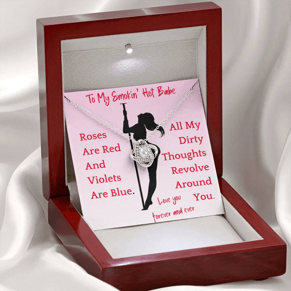 A gold-tone necklace with a pendant featuring a stylized woman holding a rose, with the text 'To My Smokin' Hot Babe' and various phrases such as 'Dirty Thoughts' and 'Love You'. The necklace is displayed in a box with a pink interior and a clear window showing the pendant and chain.